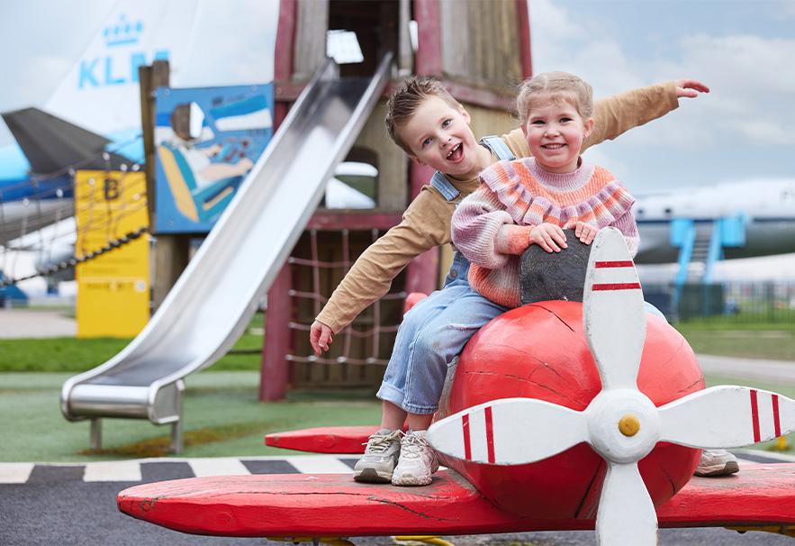 Twee kinderen zittend op een rood speelgoedvliegtuig