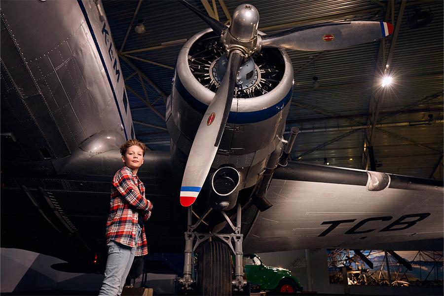 Jongetje met zijn armen over elkaar poserend voor de motor van een vliegtuig