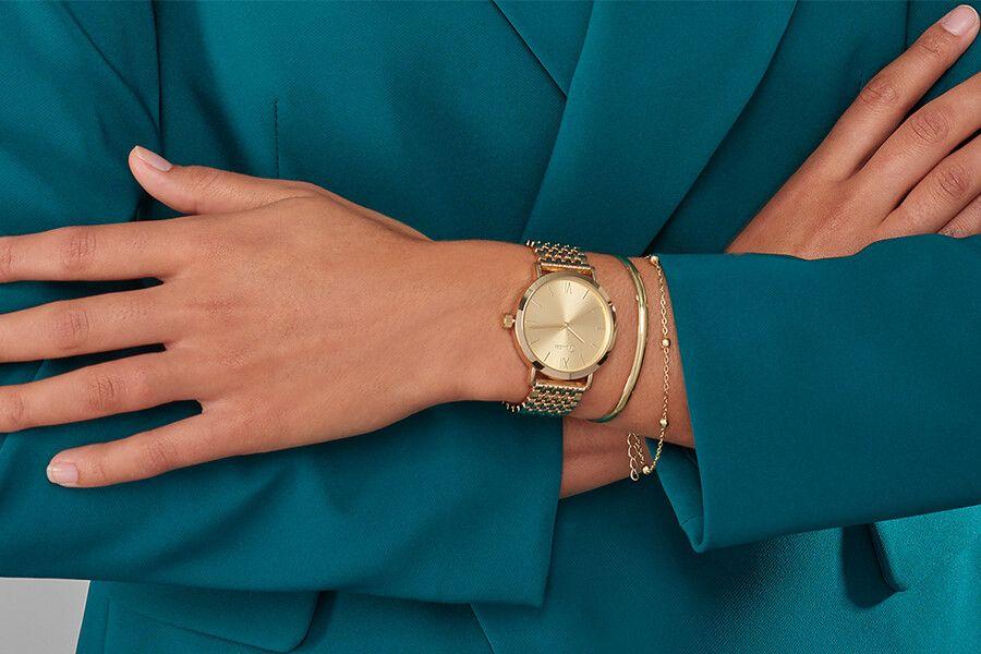 vrouwenromp met een turquoise pak aan en een goudkleurig horloge en 2 armbanden om haar pols