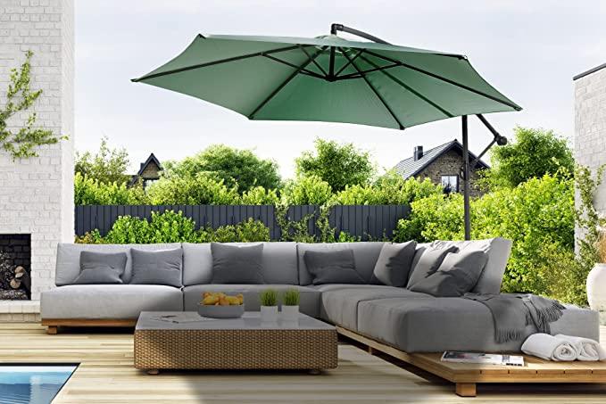 Groene zweefparasol hangt over een loungeset met een zwembad ervoor en een groene tuin