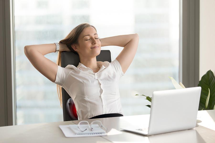een vrouw die geniet achter haar bureau van een massage van een massagekussen in haar nek