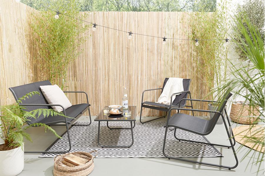 Een zwarte loungeset in de tuin met schutting (tafel, bank en 2 stoelen)