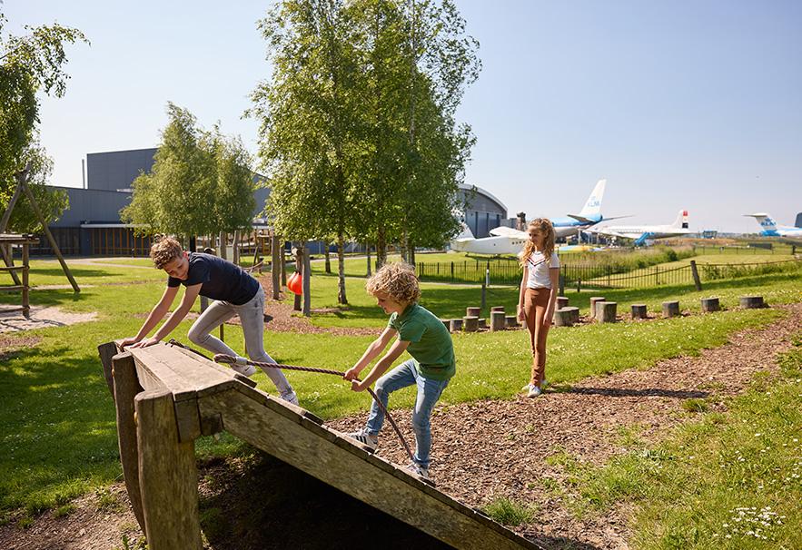Kinderen in een speeltuin met landingsbaan en vliegtuigen op de achtegrond
