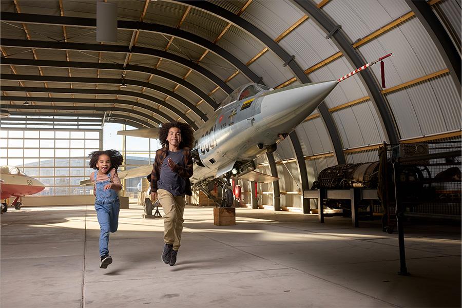 Kinderen huppelend in een loods met vliegtuig op de achtergrond