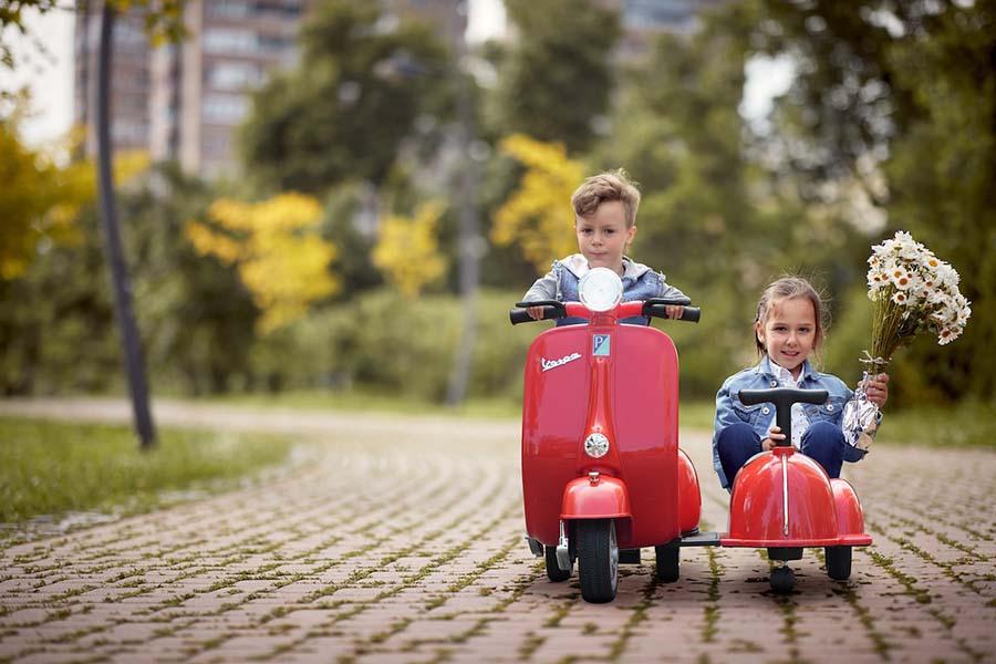 2 kinderen in rode speelgoed Vespa met zijspan
