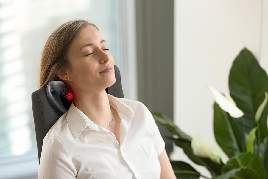 een vrouw die geniet achter haar bureau van een massage van een massagekussen in haar nek ingezoomd