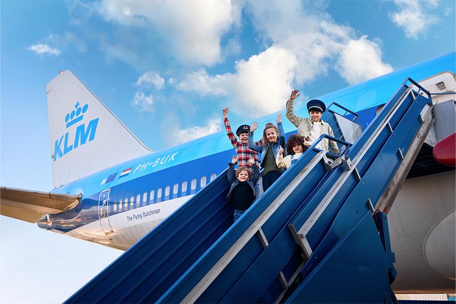 Zwaaiende kinderen vanaf de trap van een KLM-vliegtuig
